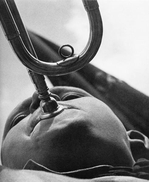A bugler with a horn, photographed from below so that the mouthpiece obscures his face