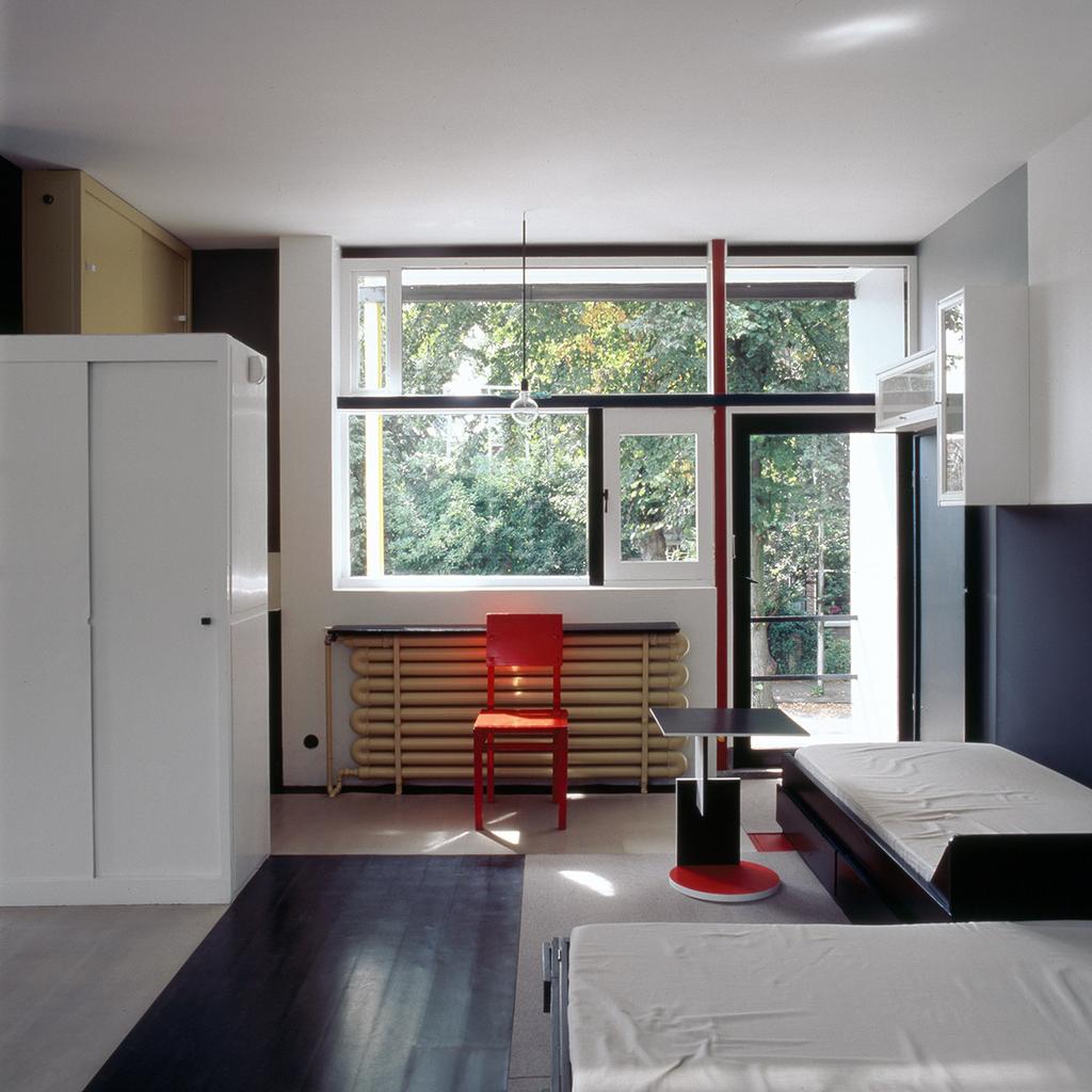 Bedroom-studio of the Schröder House with a red chair beside a tubular radiator and beds