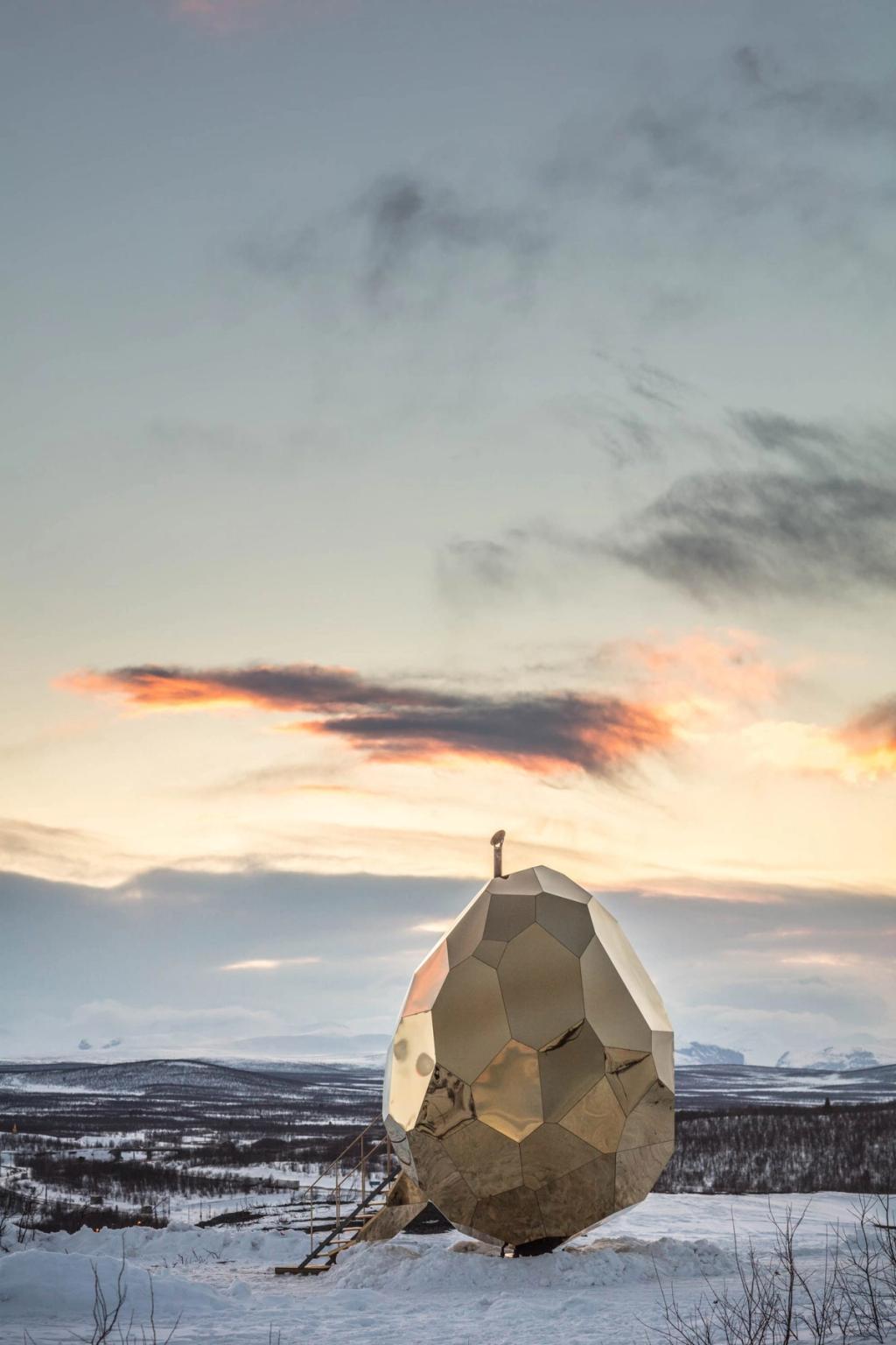 The mirrored egg-shaped Solar Egg sauna amid the snow-covered tundra of Kiruna, set against a sunset