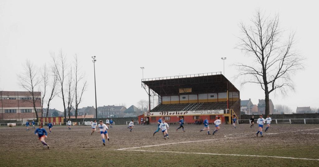 An amateur football match on a waterlogged pitch in front of an old stand on an overcast day