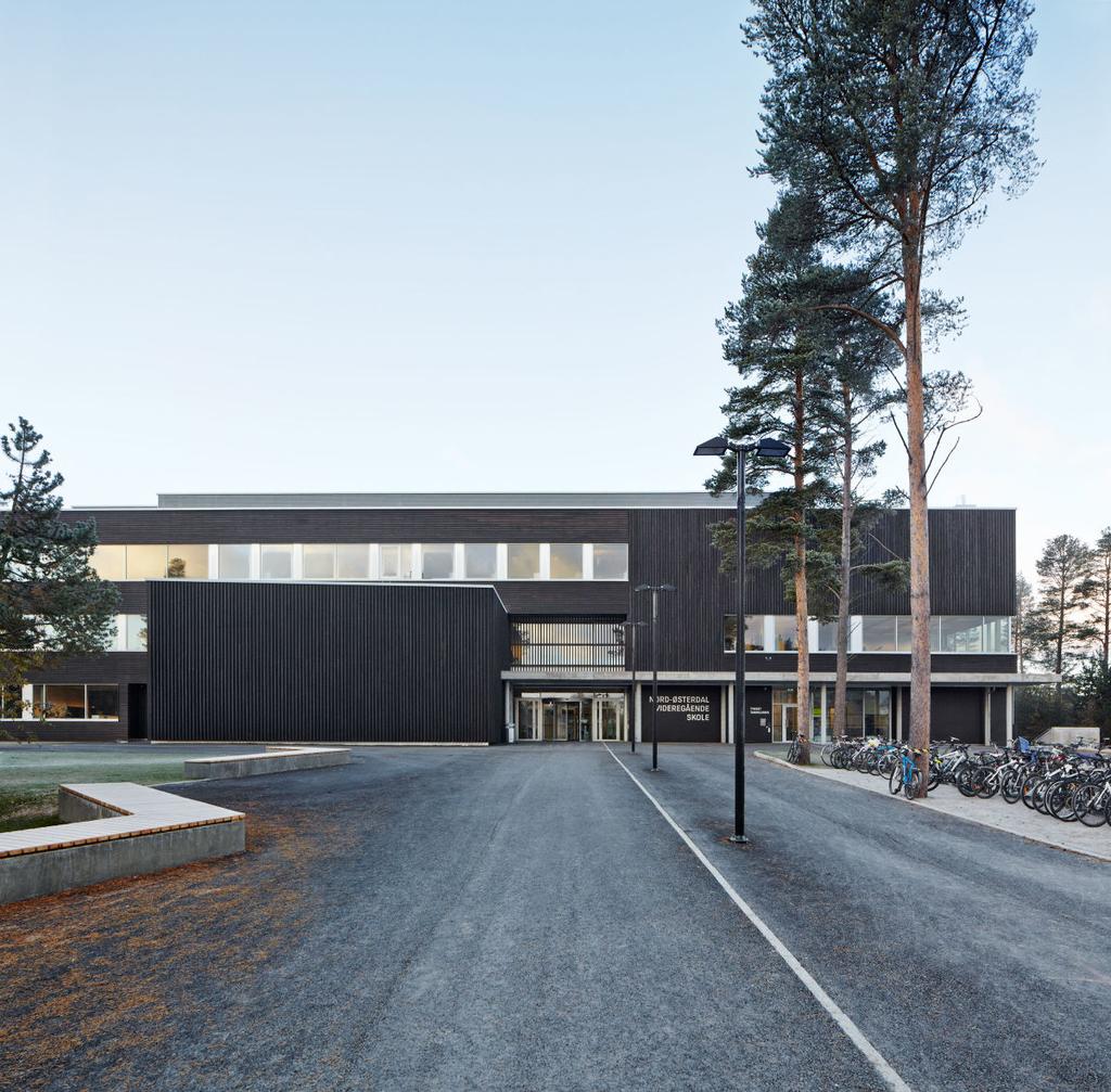 The entrance to Nord-Osterdal school, with a dark timber-batten façade set among pine trees