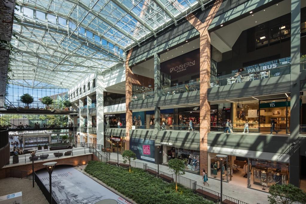 The internal atrium of Forum Gdansk with a glass roof, trees and retail galleries