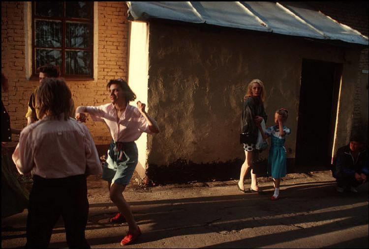 People dancing outside a brick building at sunset, a woman in a pink blouse at the centre