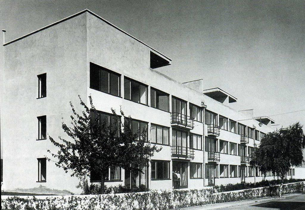 A three-storey white modernist residential building with balconies and ribbon windows