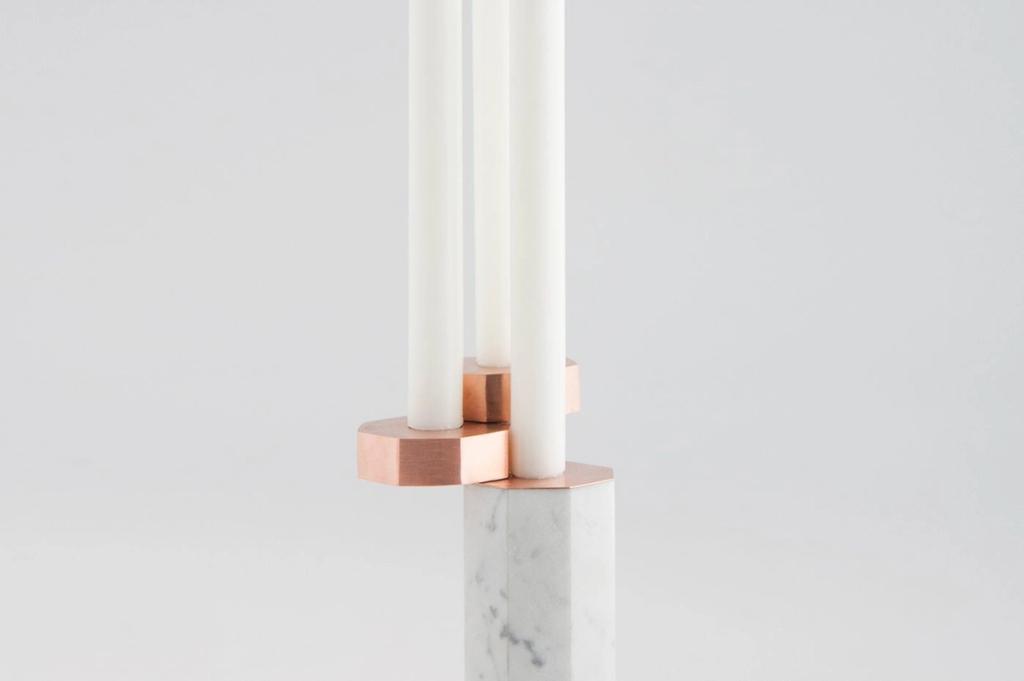 A candleholder consisting of a marble base and copper plates holding three white candles, designed by Katya Tolstykh