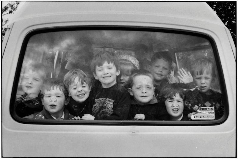 A group of children press up against the rear window of a car, pulling faces