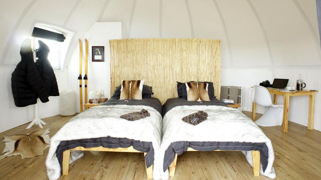 A dome bedroom with two beds covered in fur throws and skis propped against the wall