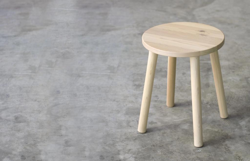 Round three-legged wooden stool on a concrete floor