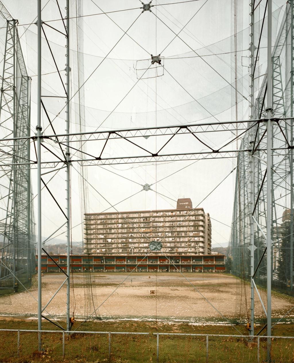 A large multi-storey building behind the tall wire fencing of a training ground