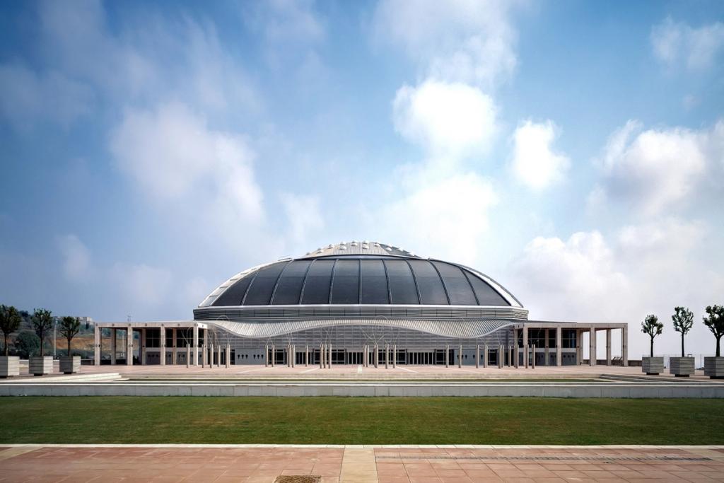The Palau Sant Jordi sports palace in Barcelona: a low-profile dome with a undulating metal roof, seen from the open plaza