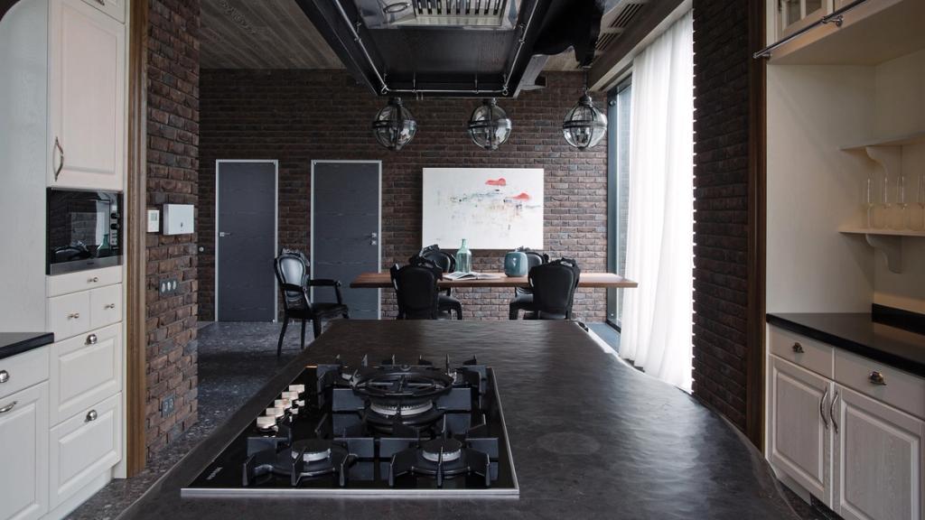 A kitchen-dining room with brick walls, a dark island with a gas hob and spherical pendant lights
