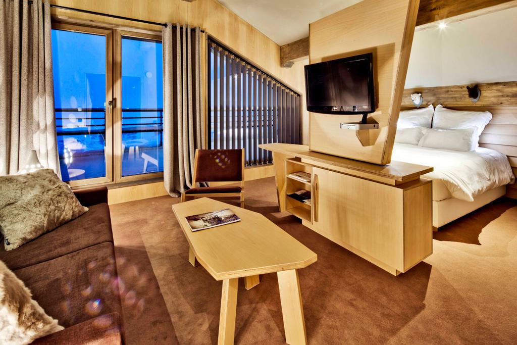A room with a bed, sofa and balcony, finished in light wood