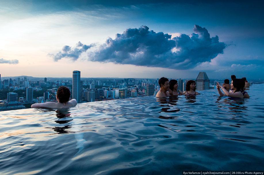 Люди фотографируются в бассейне Marina Bay Sands на фоне грозового неба над Сингапуром