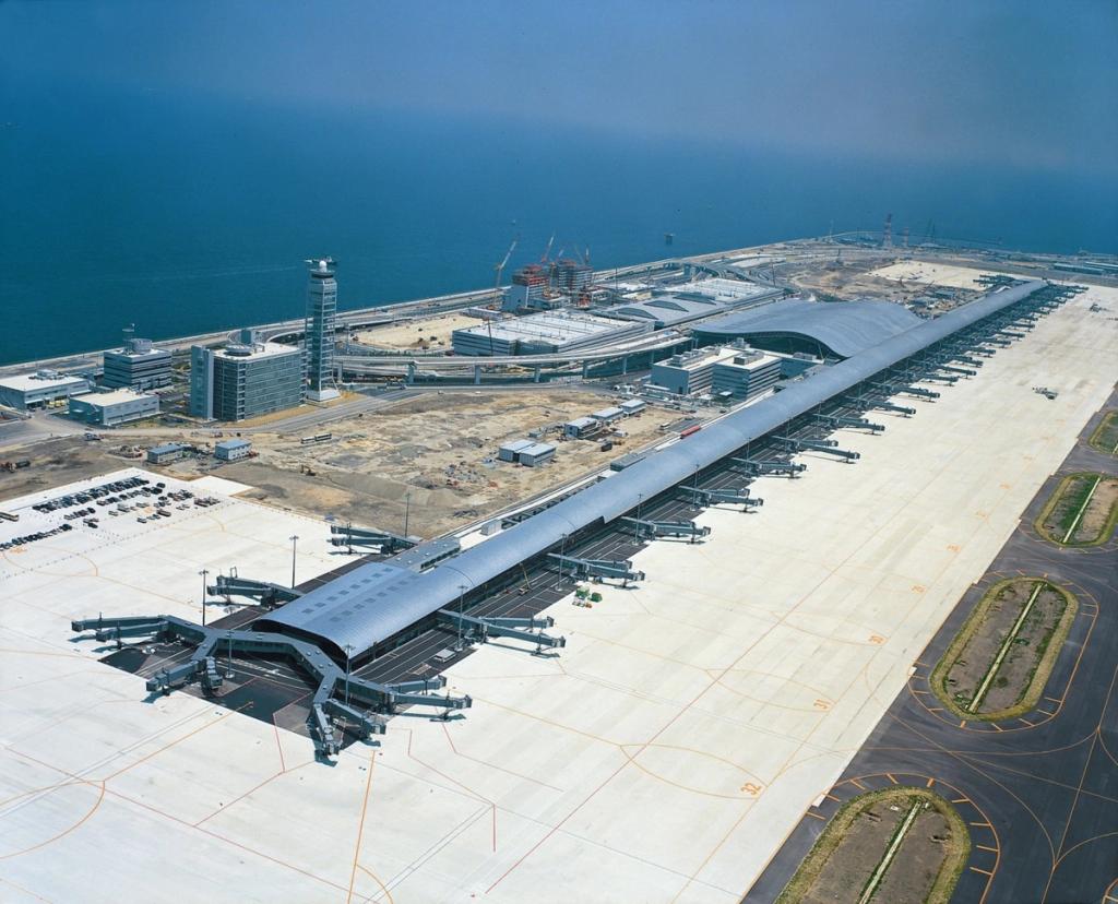 A building with a sagging cable-stayed roof and continuous glazing, set among lawns and boulders