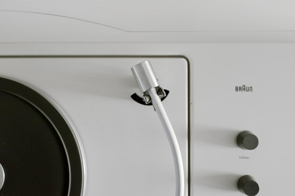 Close-up of the aluminium tonearm with its cartridge head beside the Braun logo