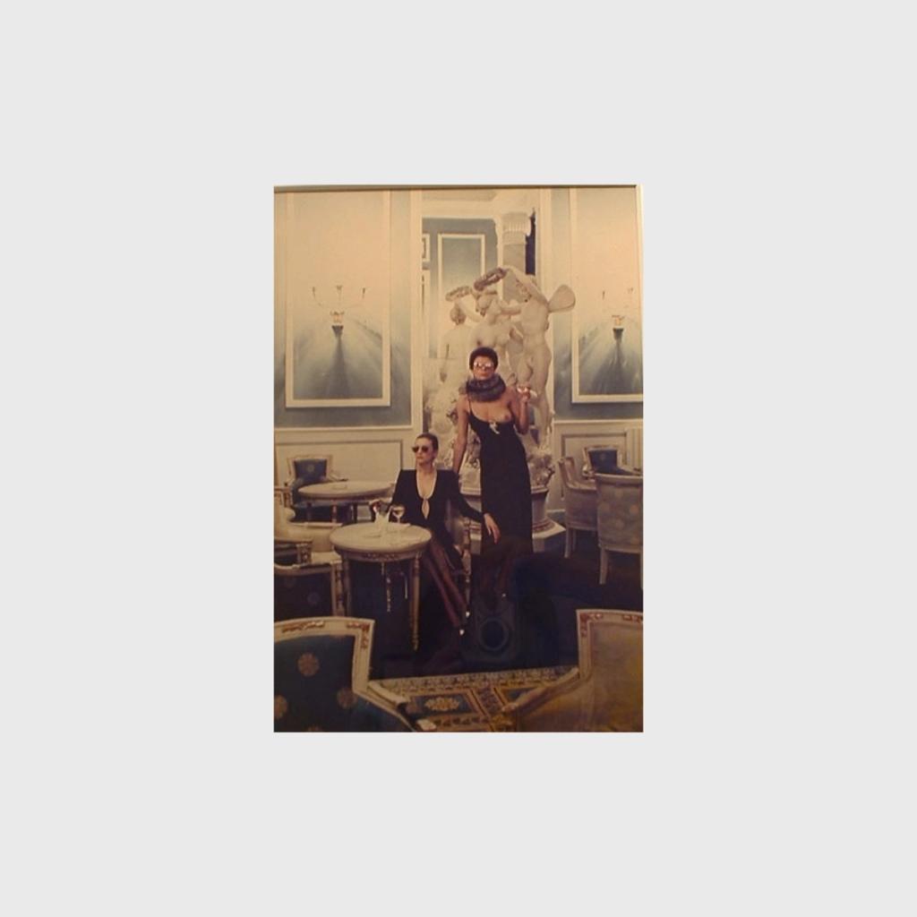 Two women in black dresses beside an antique sculpture in a luxurious interior, colour frame