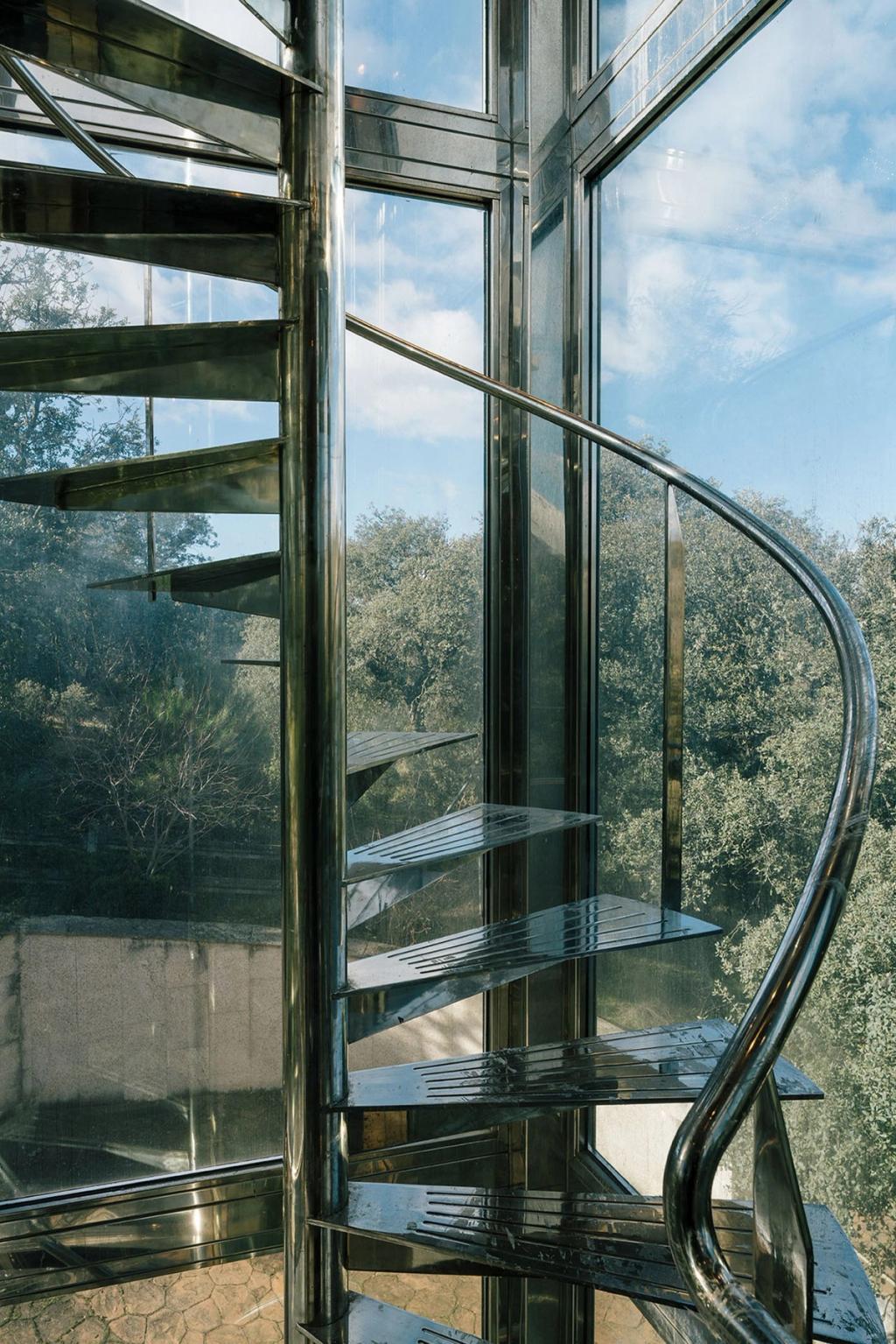 A steel spiral staircase behind a glass façade overlooking an oak forest
