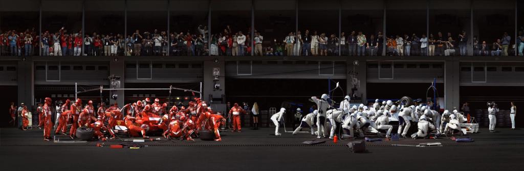 Formula 1 pit-stop panorama: a team in red on the left and a team in light-coloured overalls on the right