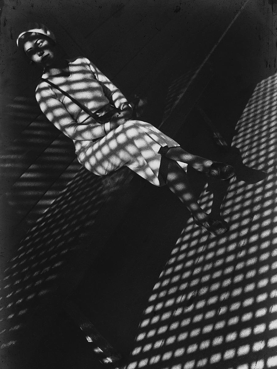 A seated woman in striped clothing, caught in the lace-like shadow of a grille