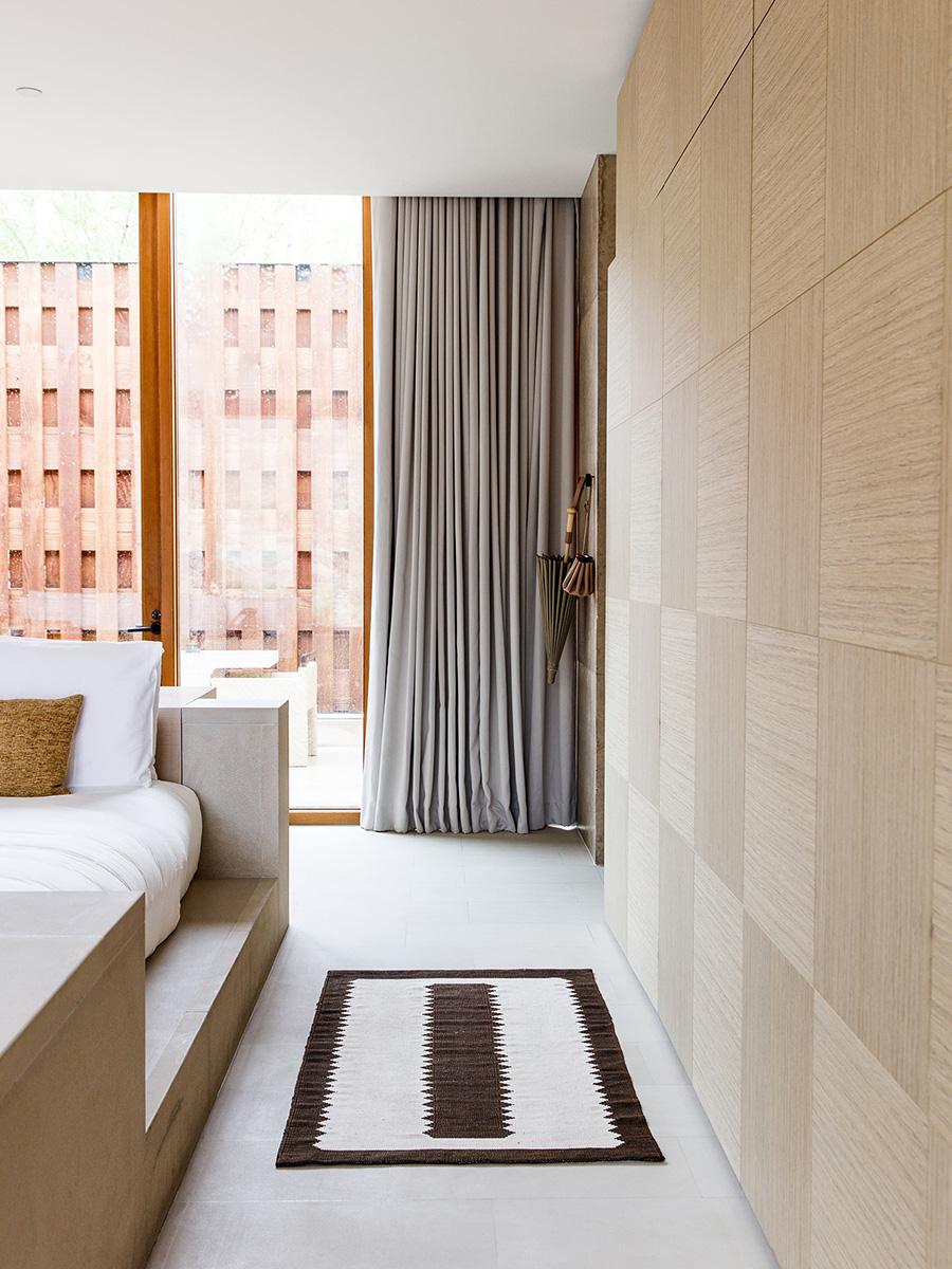 Interior of an Amangiri room featuring a light wooden wardrobe and a brown-and-white rug beside a panoramic window