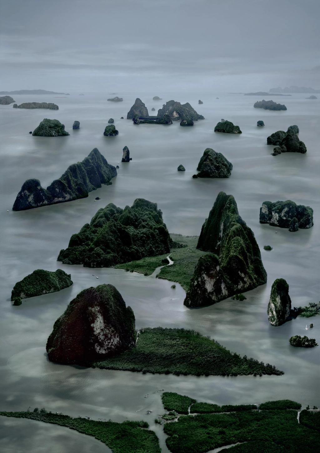 Numerous forested karst islands in a calm grey sea, seen from a bird's-eye view