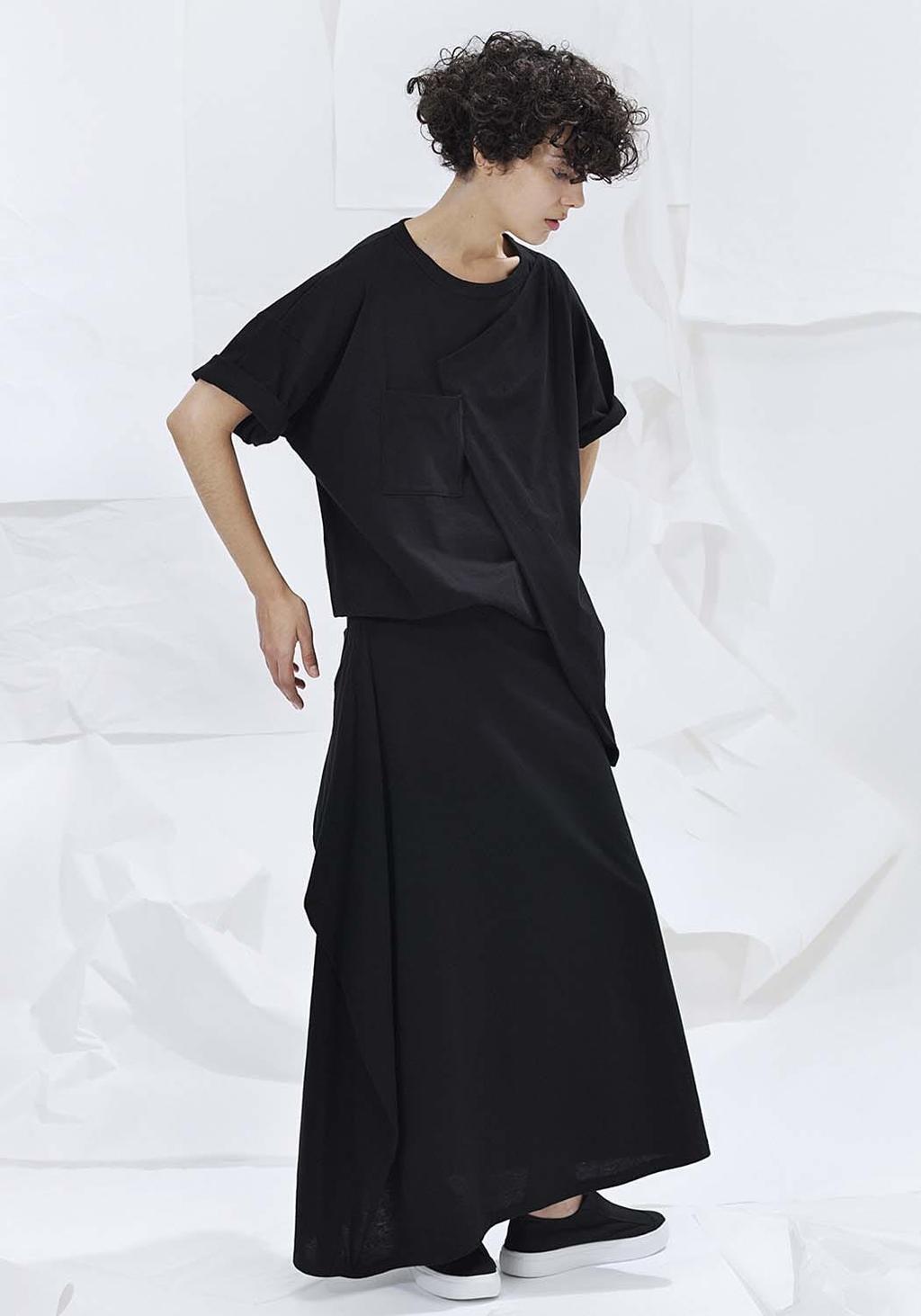 A model in a loose black T-shirt with a pocket and a long black skirt