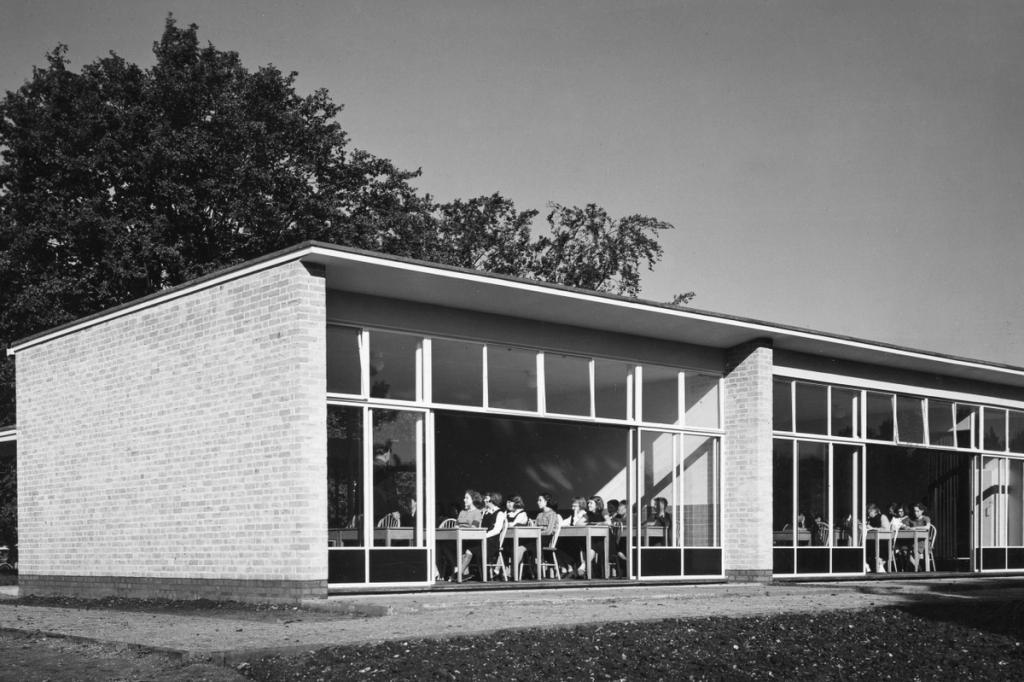 A single-storey pavilion in light brick with continuous glazing, people seated at tables inside