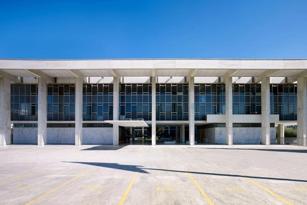 Façade of the US Embassy in Athens: a marble colonnade in front of a glazed block beneath a blue sky
