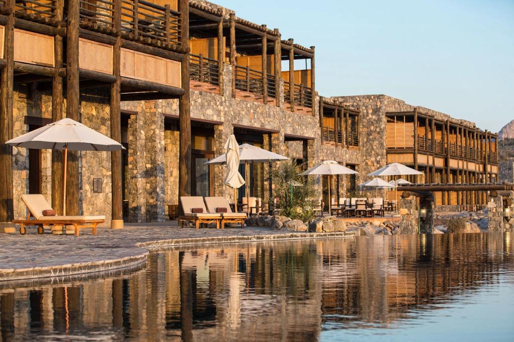 The stone buildings of Alila Jabal Akhdar with parasols and an infinity pool at sunset