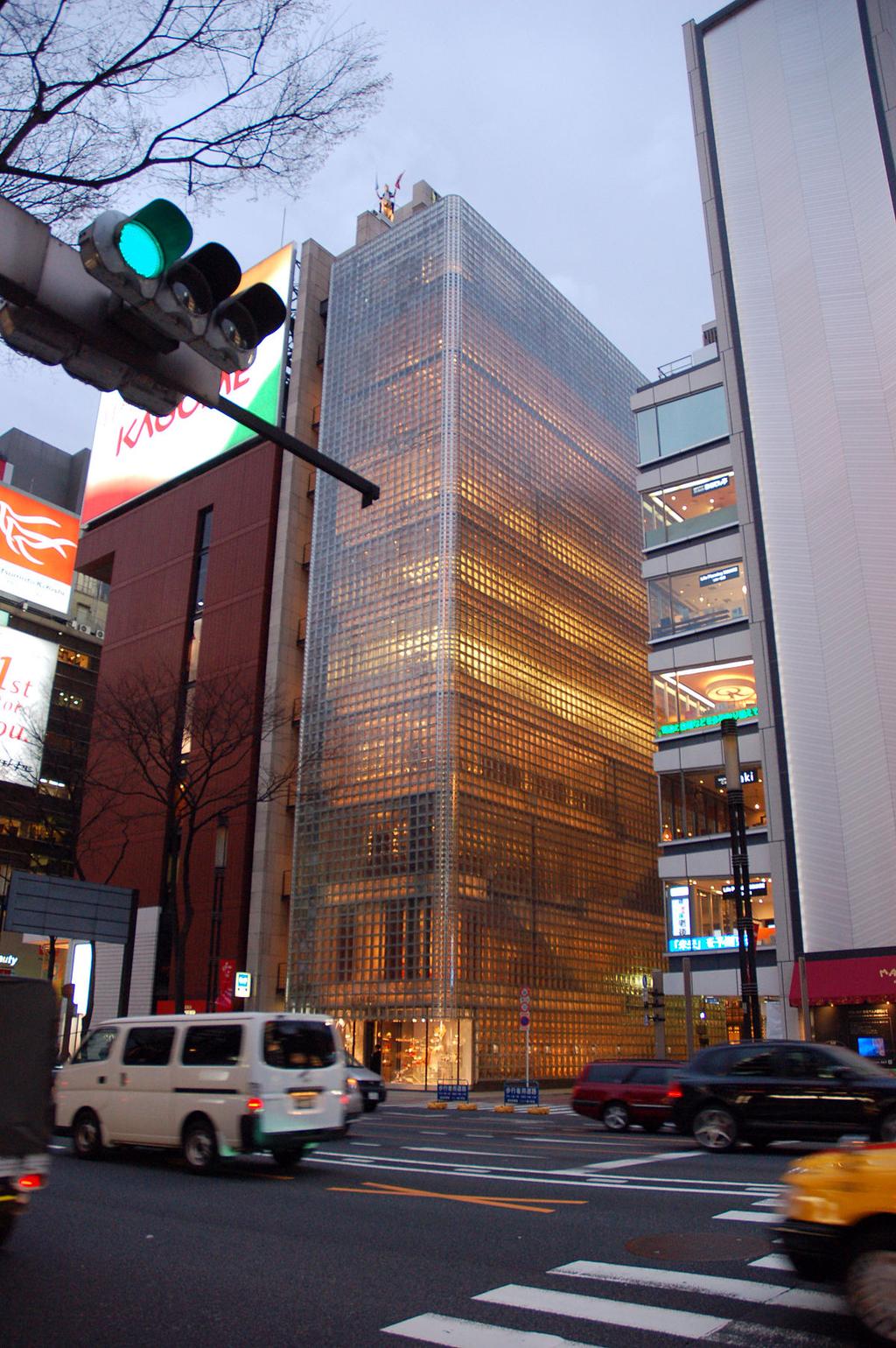 The slender glass tower of Maison Hermès in Tokyo, glowing above an intersection in the evening