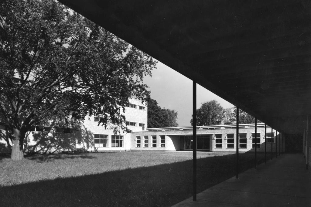 A low brick building with ribbon glazing and a canopied gallery supported on columns