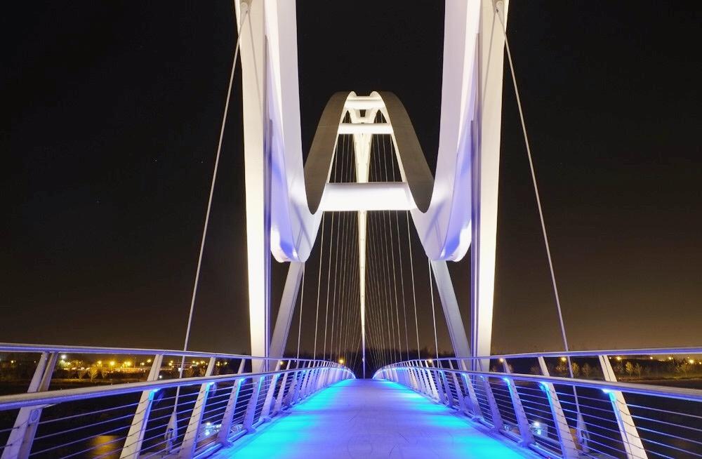 The Infinity Bridge in England at night, with blue-lit decking and white inclined pylons