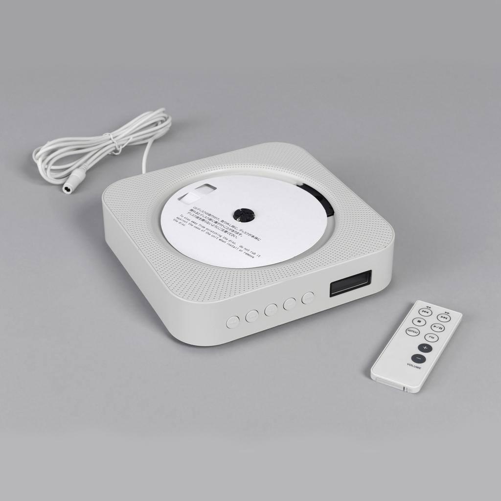 MUJI CD player lying on a grey surface beside a white cord and remote control