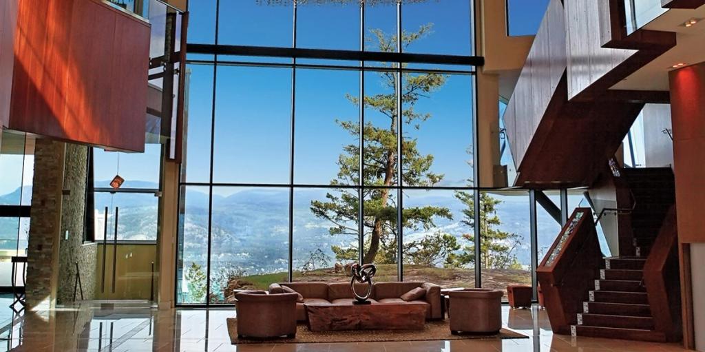 A double-height lobby with a panoramic window, a pine tree and views of the mountains and Okanagan Lake