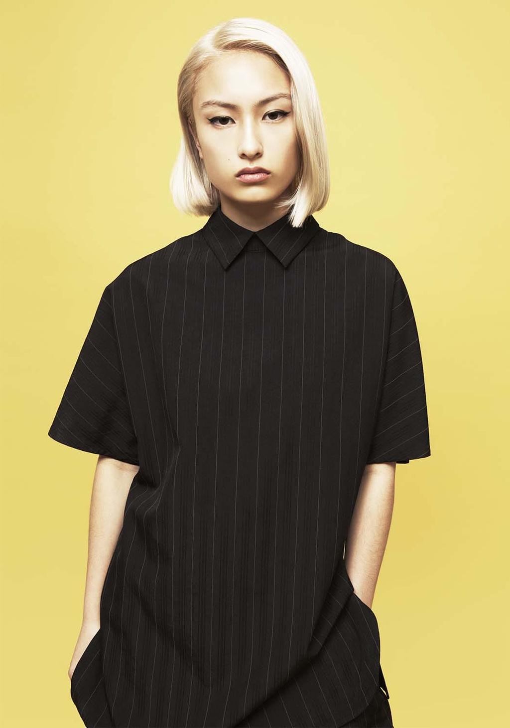 Portrait of a blonde woman in a black fine-stripe shirt against a yellow background