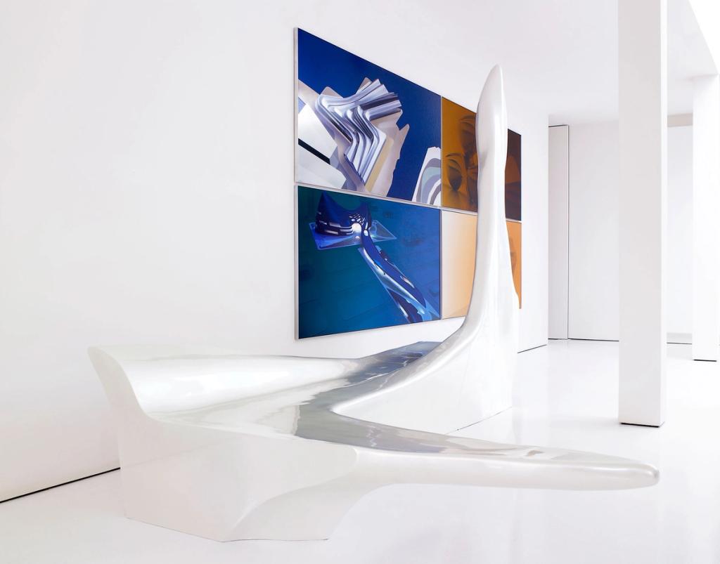 A glossy white wave-form bench in a white hall against a backdrop of abstract paintings