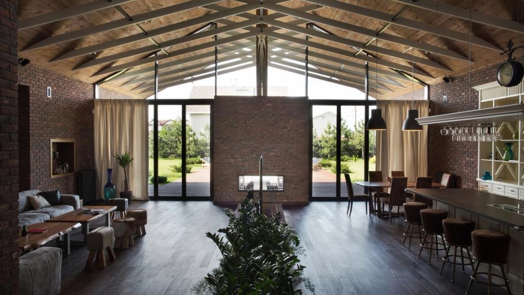 The main open-plan space beneath a double-pitched timber roof, with a bar counter and panoramic access to the garden