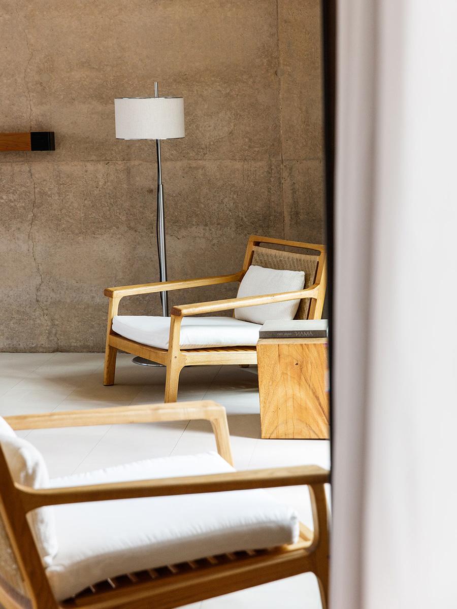 Wooden armchairs with light cushions and a floor lamp beside a concrete wall in a room at the Amangiri hotel