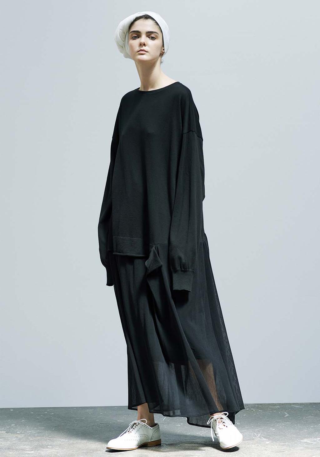 A model in a long oversized black dress, white beret and white shoes