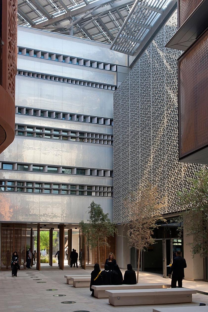 A Masdar City courtyard with perforated walls, trees and people sitting on benches