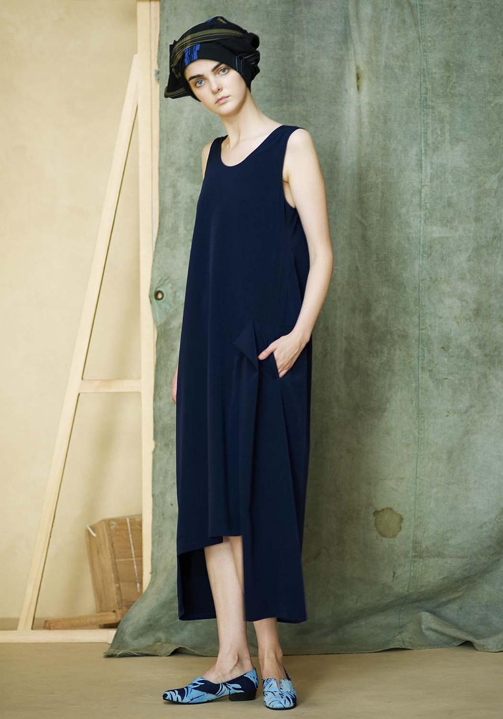 A model in a dark navy sleeveless dress and a patterned turban beside a draped backdrop