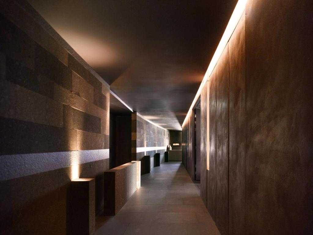 A dark corridor with illuminated stone walls and low stone benches