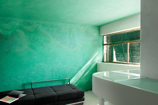 A turquoise room with textured walls, a black bench by a window with blinds