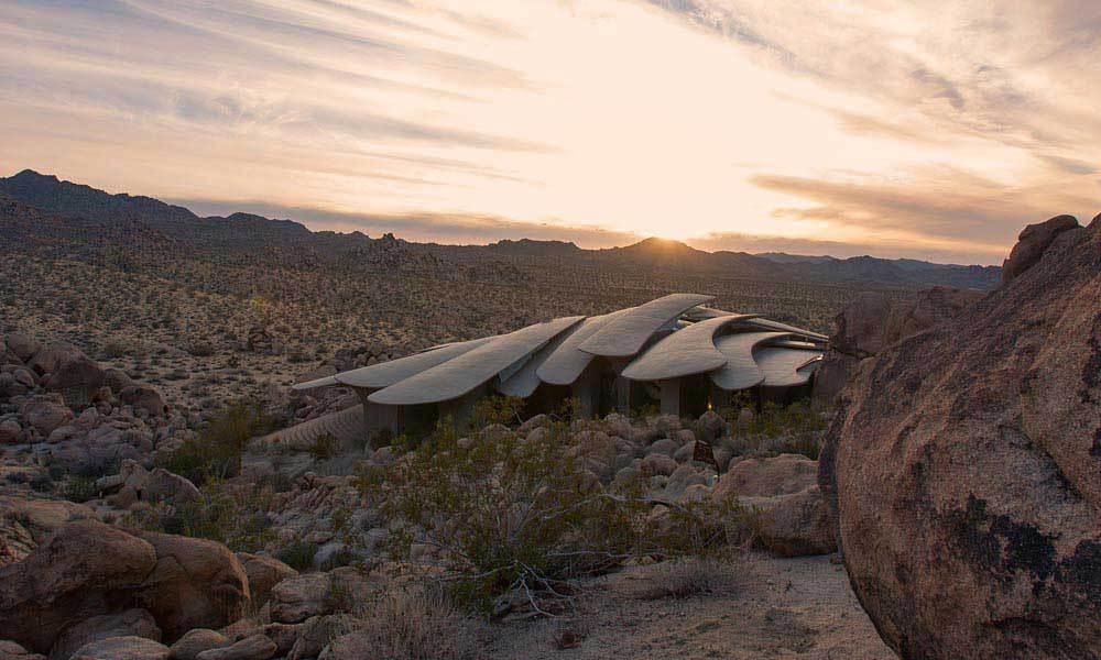 A shell-like house of concrete petals nestled into a rocky desert landscape at sunset