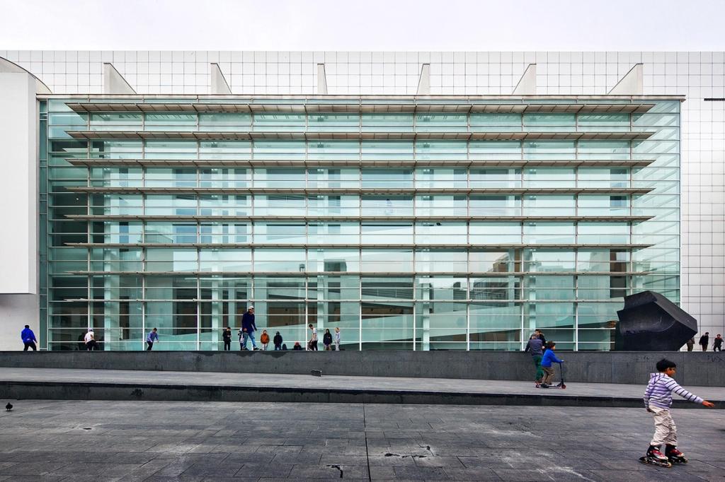 Закруглённый стеклянный вестибюль MACBA с пуфами на тёмном полу, Барселона