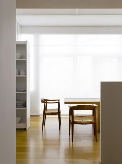 A dining area with two wooden chairs by a window with a frosted blind and an open shelving unit