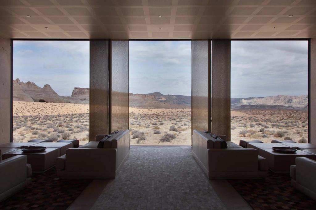 A living room with tall windows in black frames looking out onto a forest