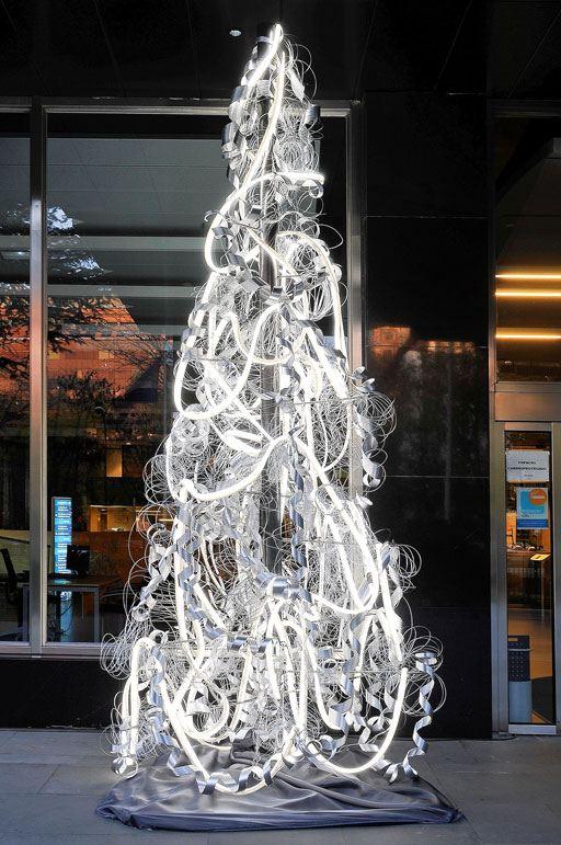 A tree made of glowing neon tubes in front of a dark glazed façade at night