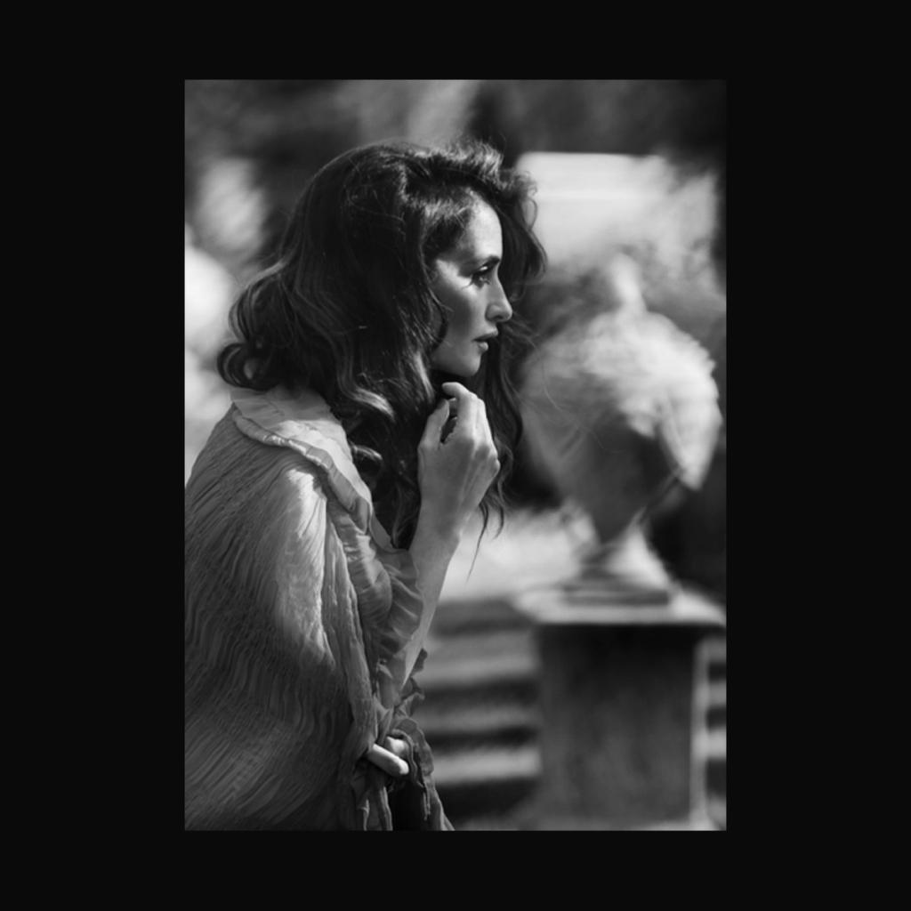A black-and-white profile of a dark-haired woman in a garden beside a stone urn