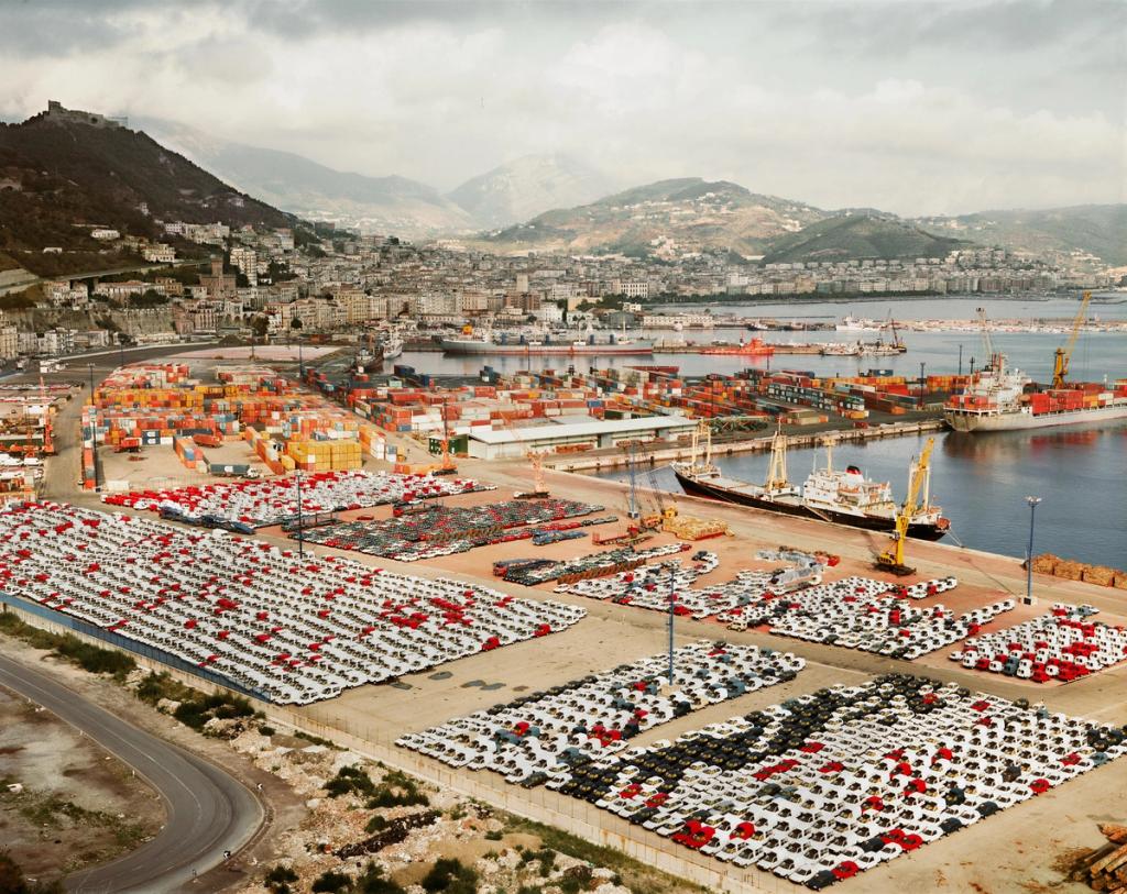 A seaport with thousands of new cars and containers against the backdrop of a coastal city